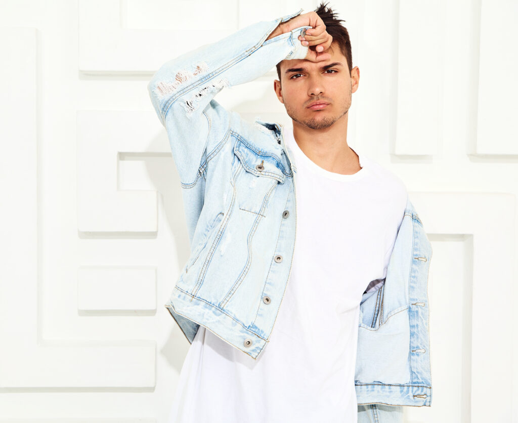 portrait of handsome young model man dressed in jeans clothes posing near white textured wall